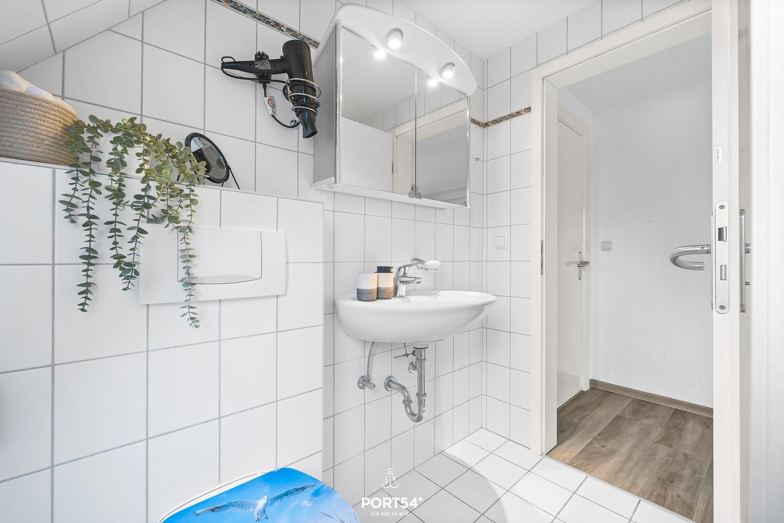 Badezimmer mit Waschbecken, Spiegel und Haartrockner an der Wand.