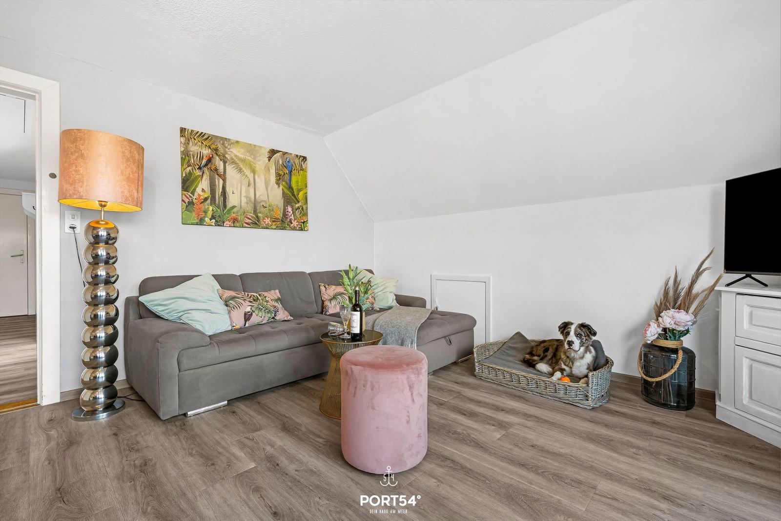 Wohnzimmer mit Sofa, Fernseher und Hundebett. Holzfußboden und Wandbild.