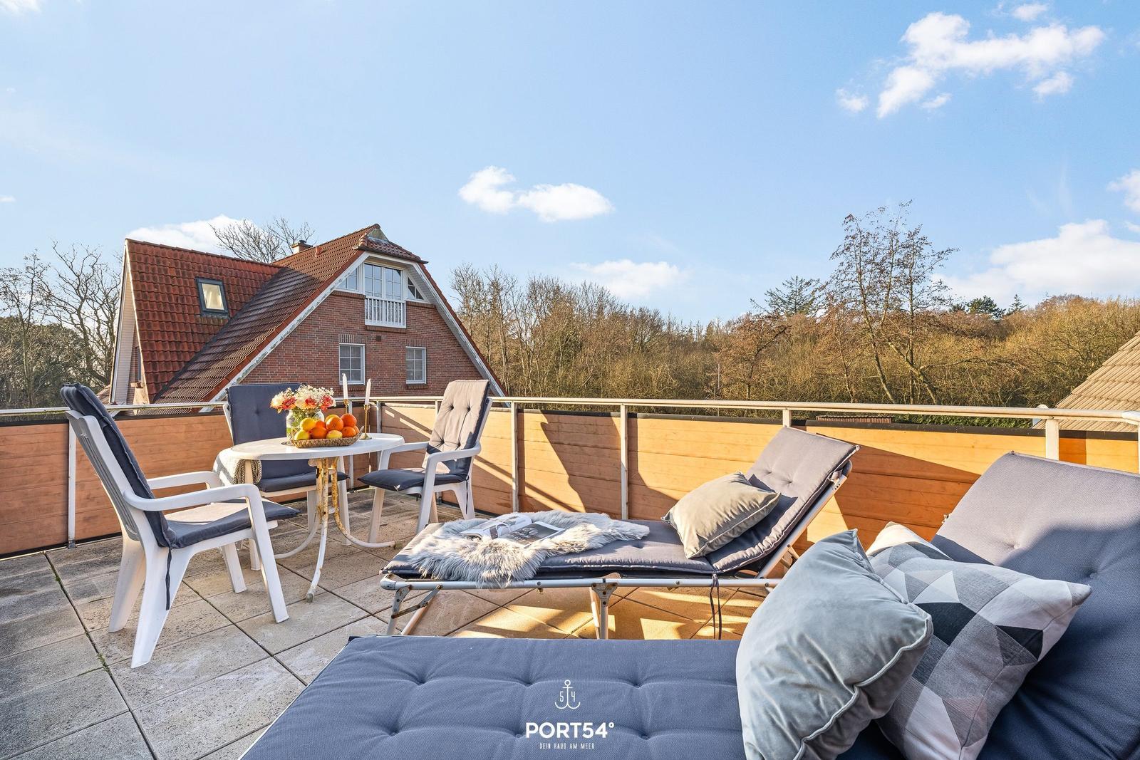 Terrasse mit Liegestühlen, Tisch und Sicht auf Haus und Wald.