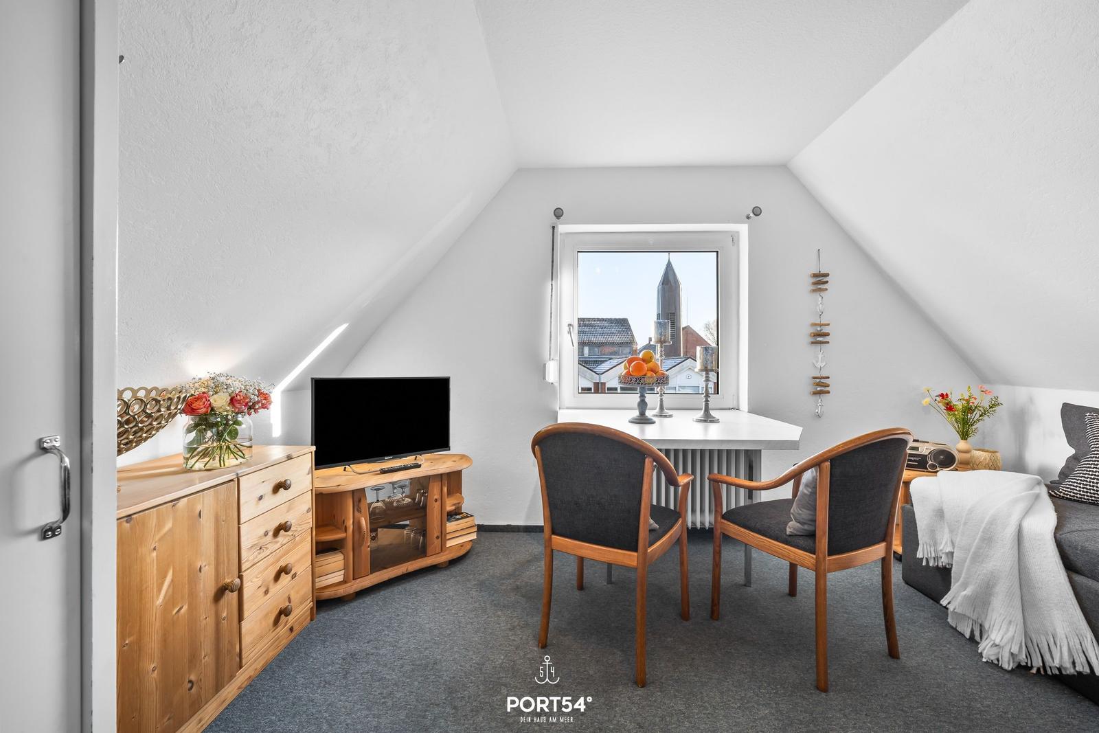 Dachgeschosszimmer mit TV, Schreibtisch und Fensterblick auf Kirchturm