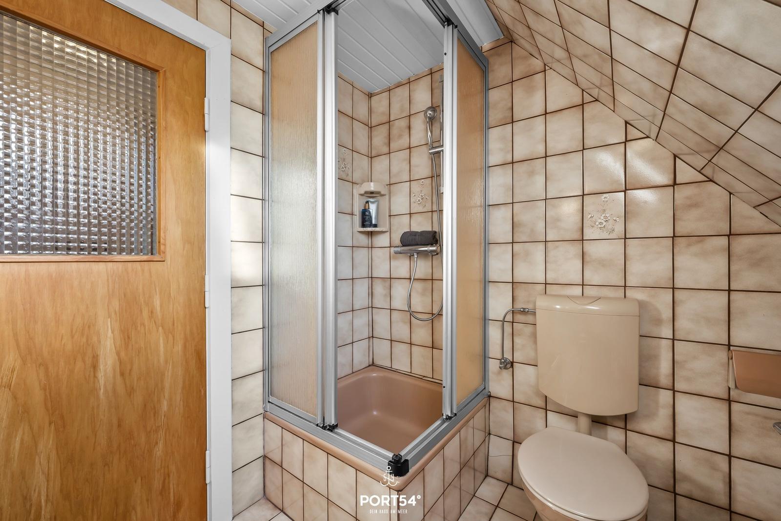 Badezimmer mit Dusche, Toilette und Holztür mit Glassteinfenster.
