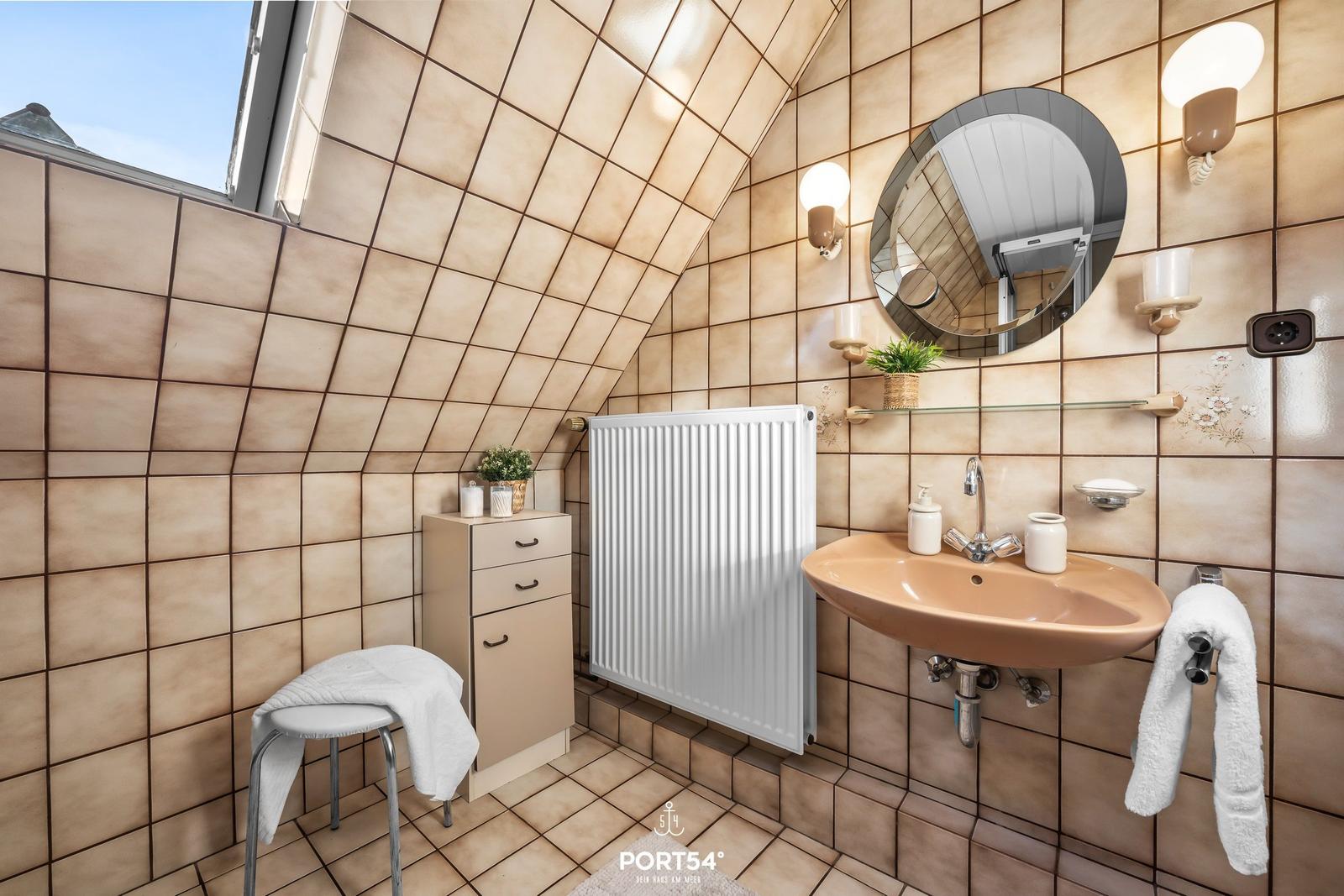 Badezimmer mit Dachschrägen, Waschbecken, Spiegel und Heizkörper.
