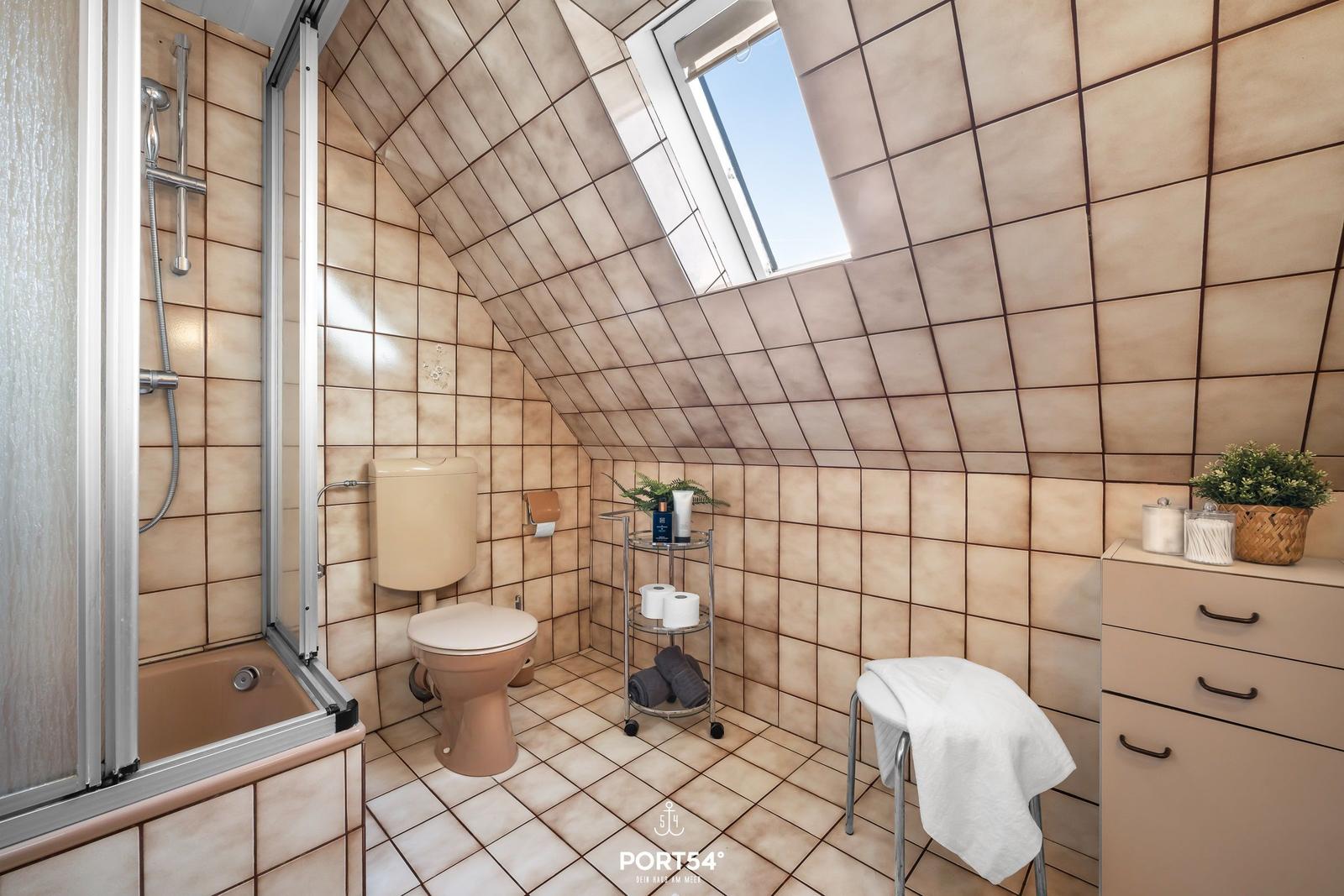 Badezimmer mit Dusche, Toilette und Dachfenster. Fliesenwand und -boden.