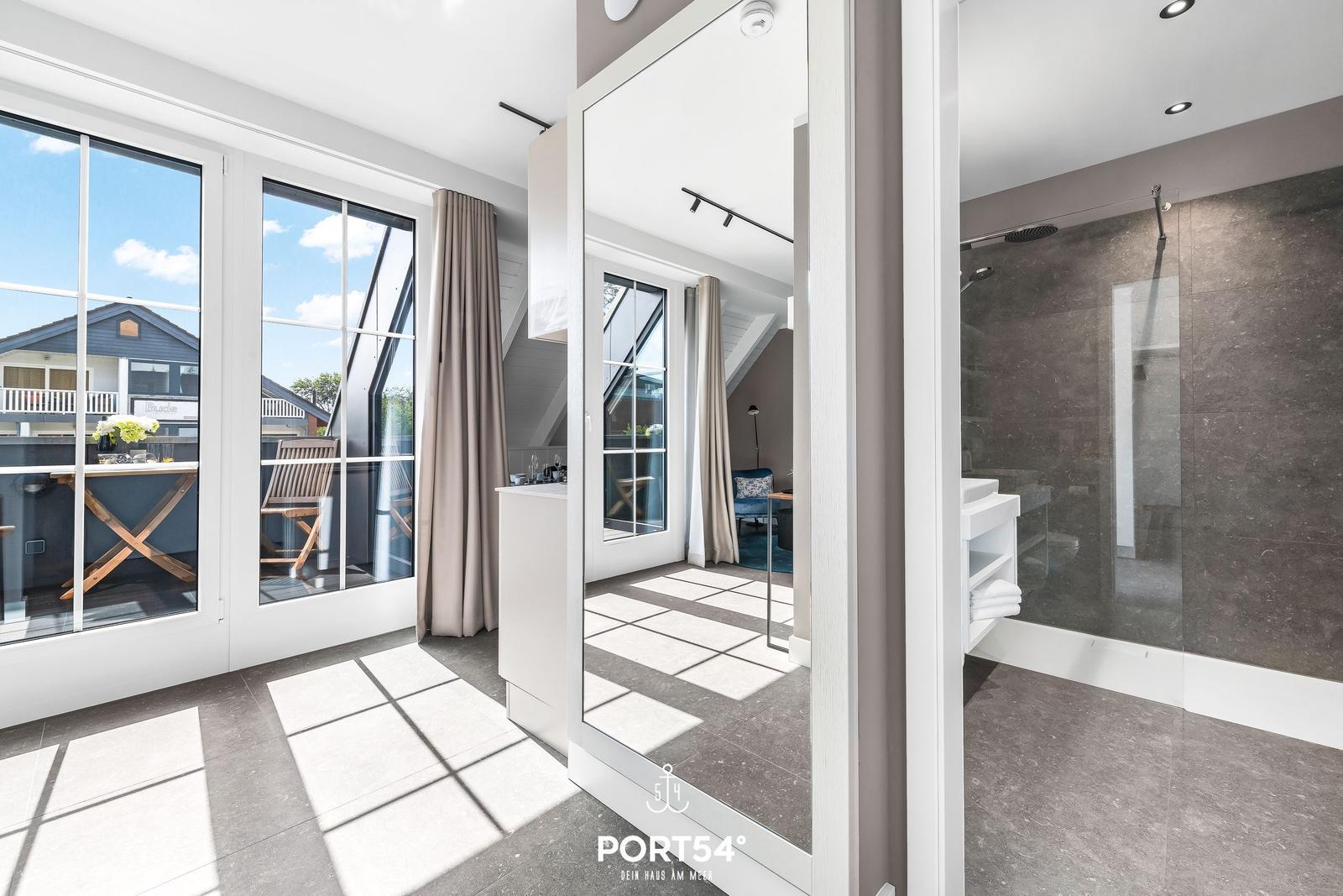 Badezimmer mit Dusche und Blick auf Terrasse mit Tisch und Stühlen.