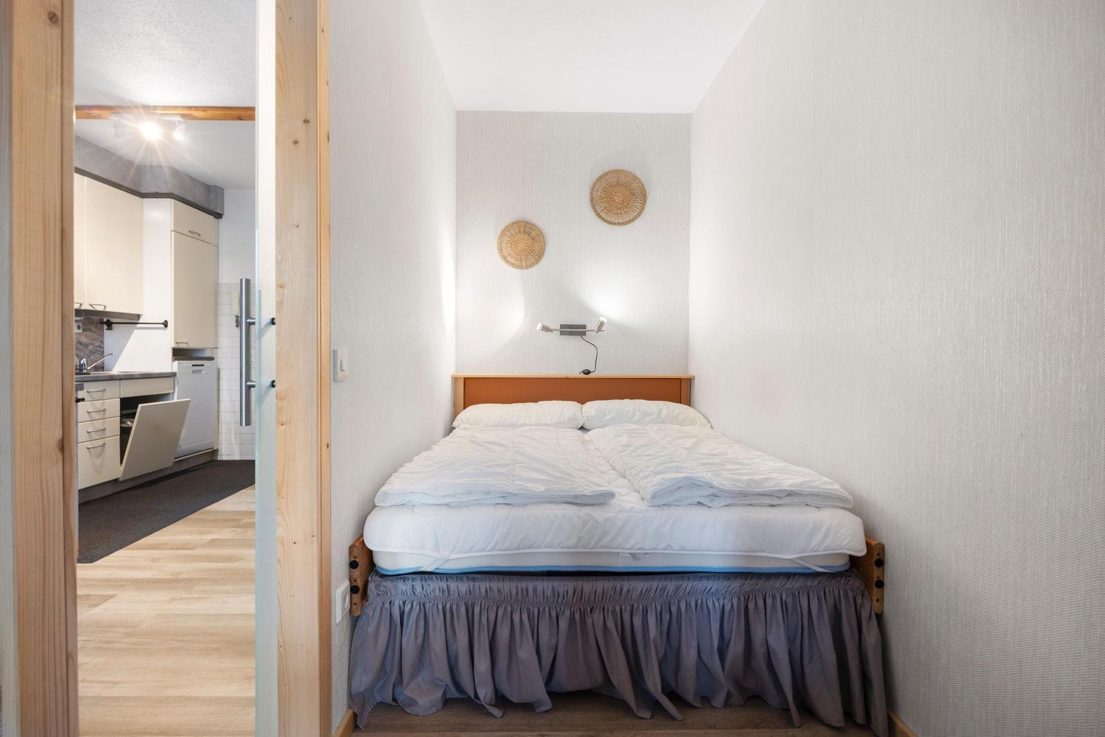 Schlafzimmer mit Doppelbett und Küchenbereich im Hintergrund.