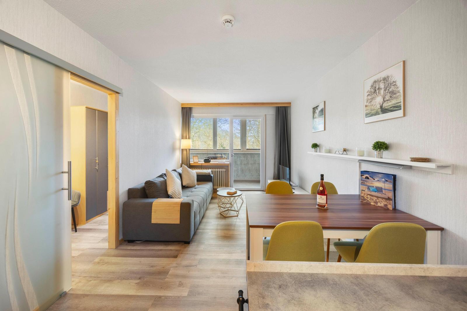 Wohnbereich mit Sofa, Esstisch und Balkontür.