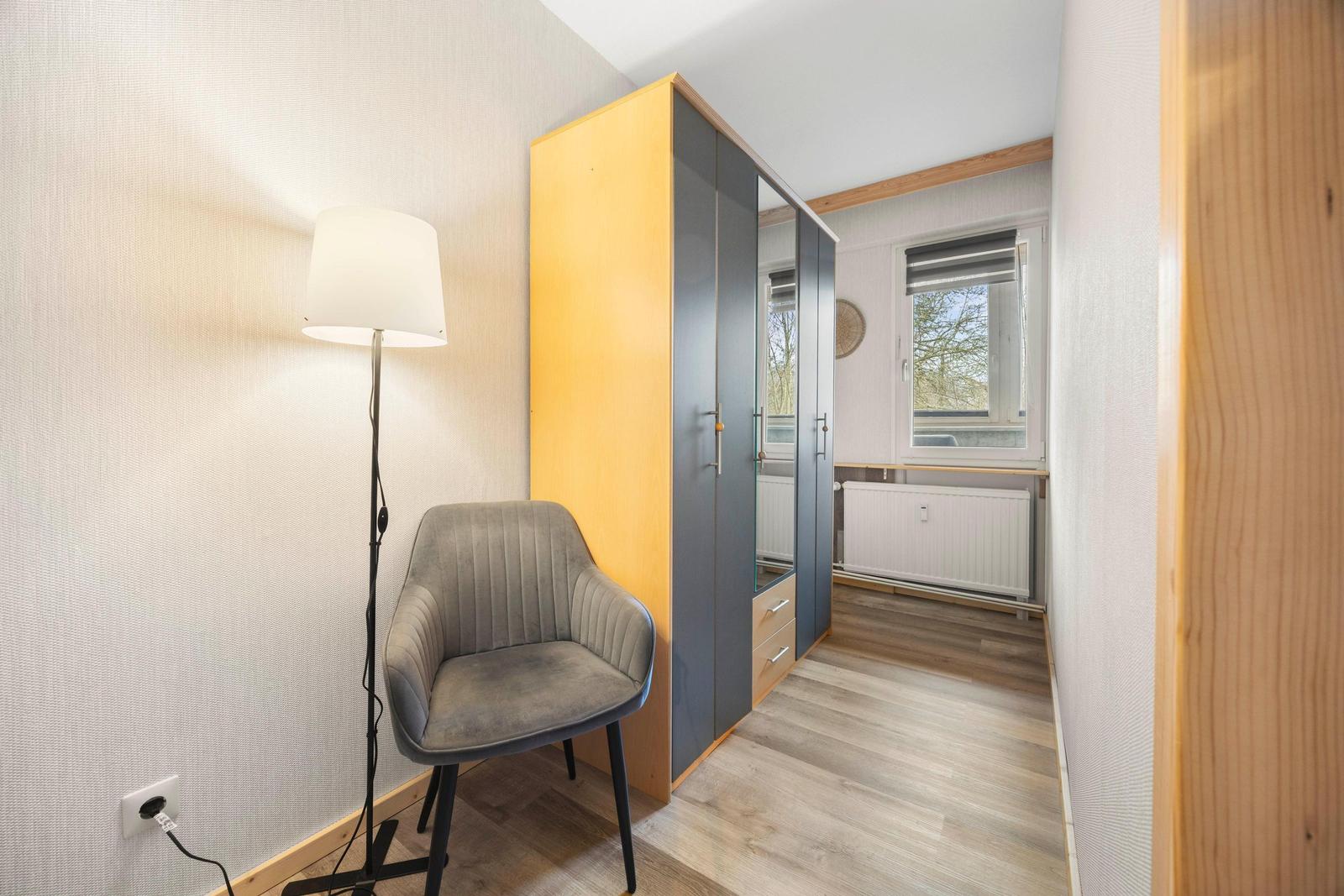 Schlafzimmer mit Kleiderschrank, Stuhl und Stehlampe. Fenster mit Blick nach draußen.