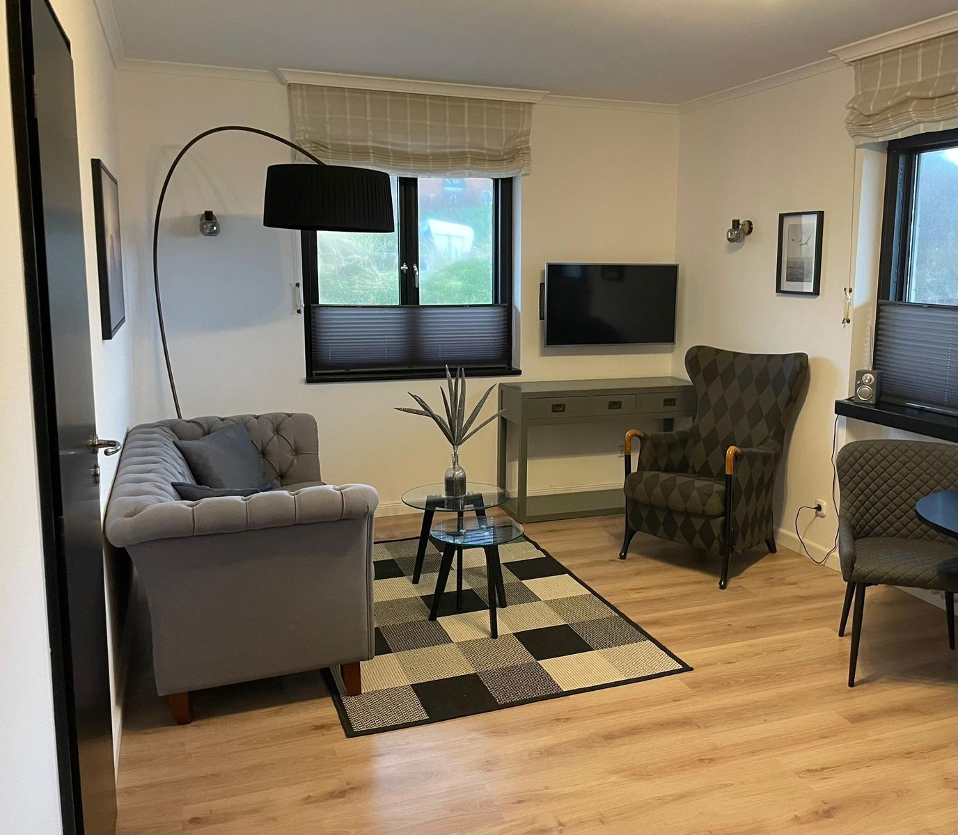 Wohnzimmer mit Sofa, Sessel und TV. Holzboden und Teppich.