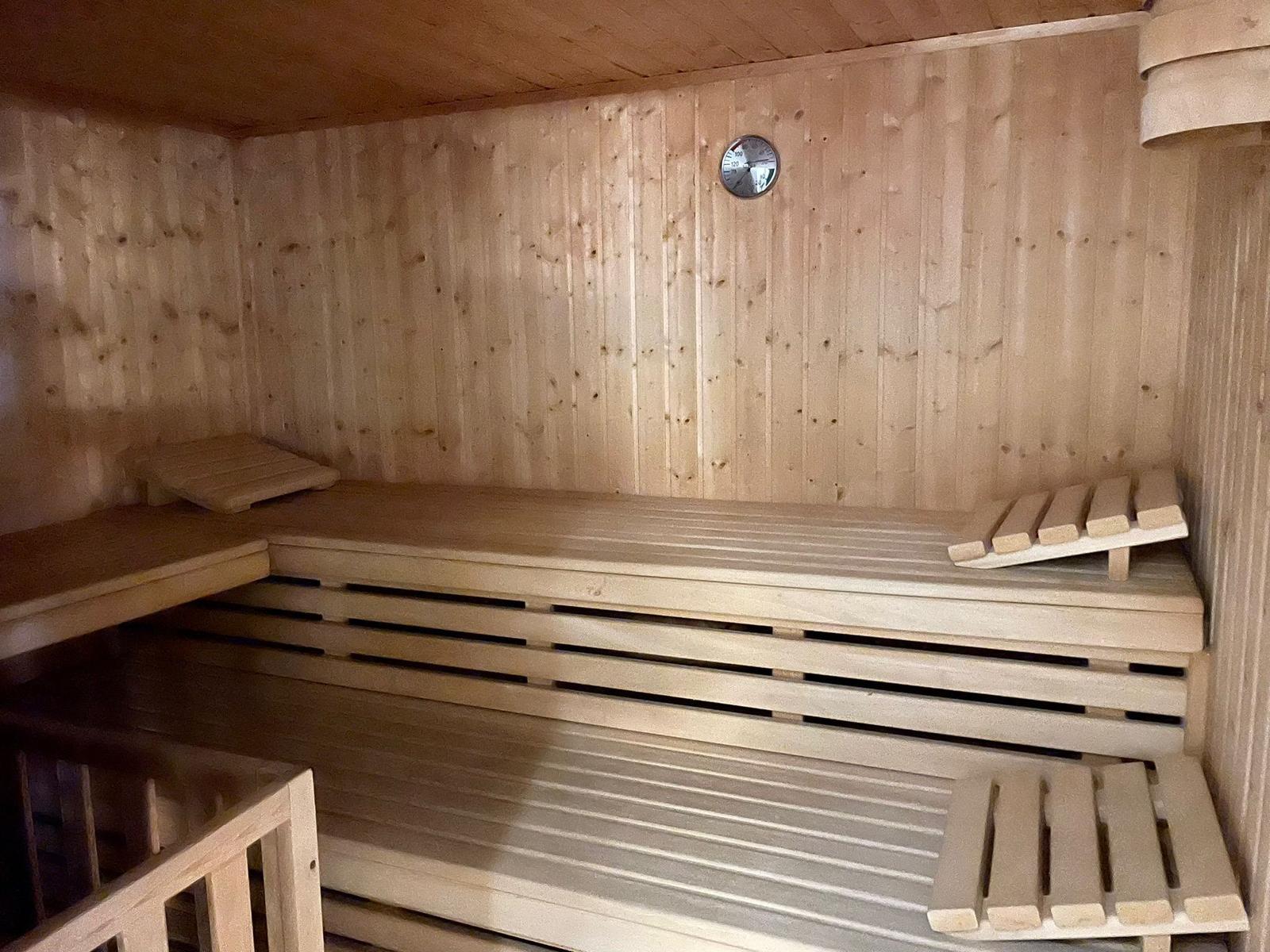 Holzsauna mit Sitzbänken und Temperaturmessgerät an der Wand.