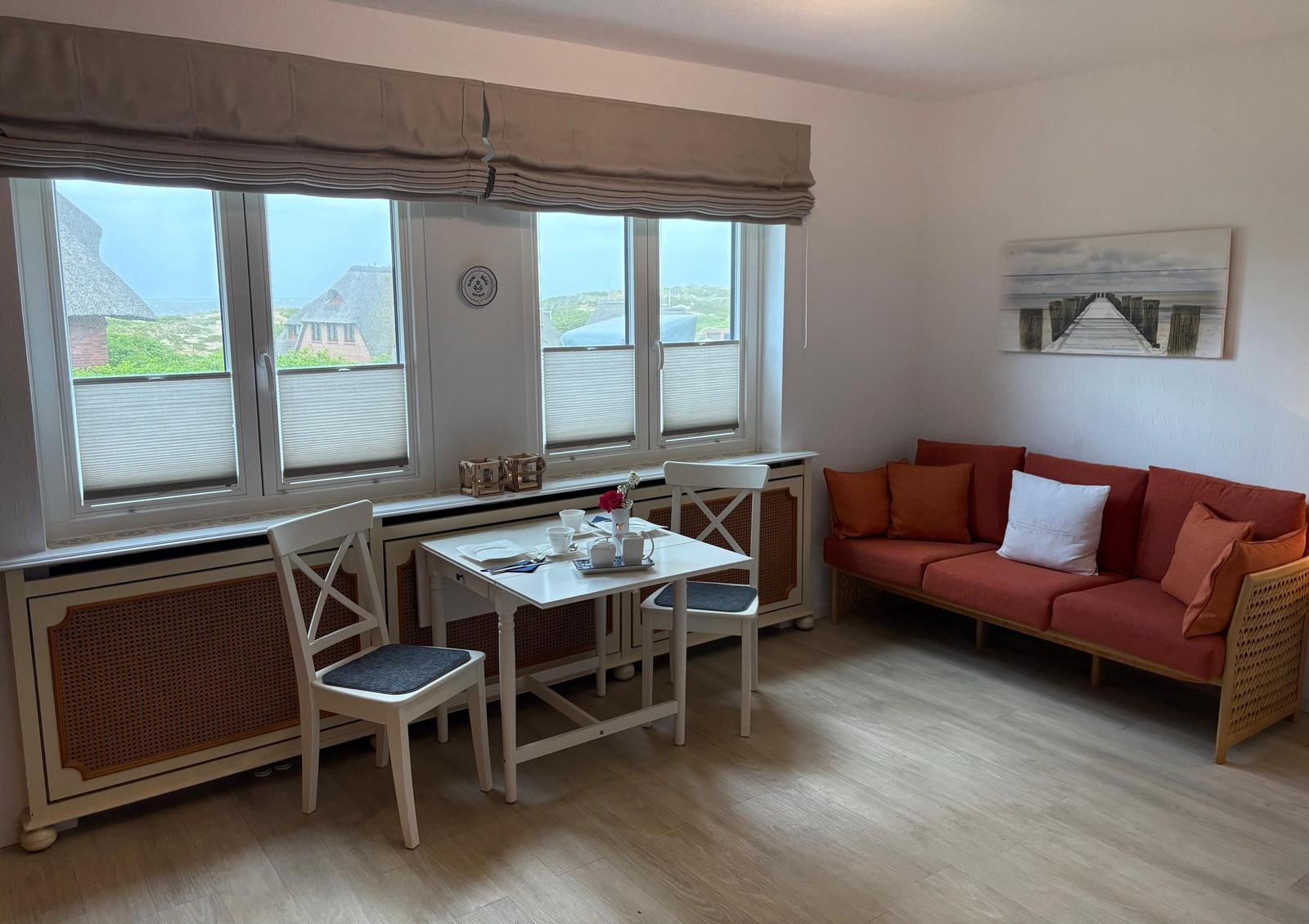 Wohnzimmer mit Sofa, Esstisch und Fensterblick auf Dächer