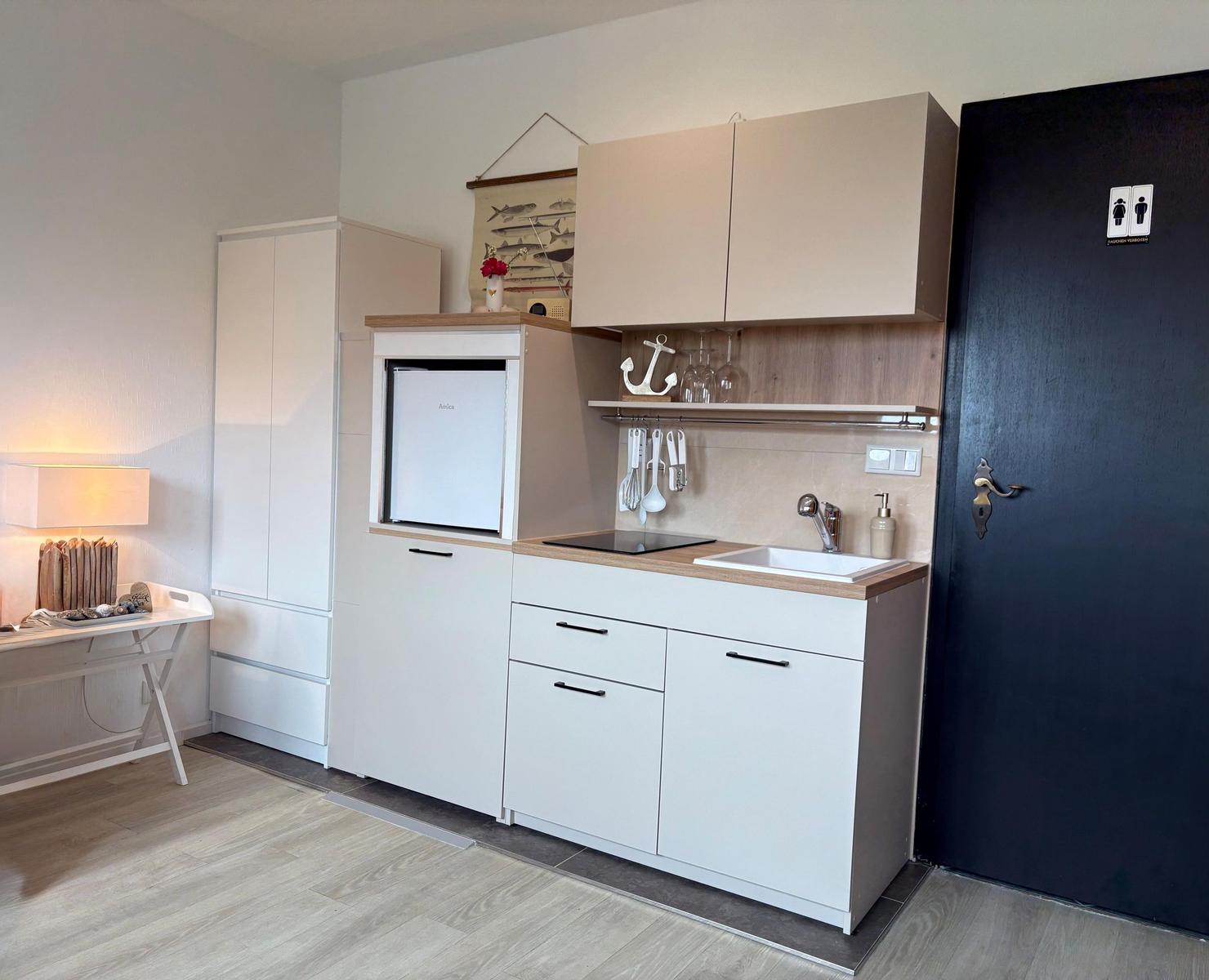 Küche mit Kühlschrank, Spüle und Küchenschränken. Nebenraum mit Schreibtisch und Lampe.