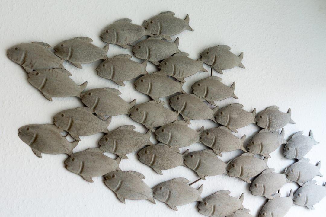 Wanddekoration mit Fischfiguren aus Metall an einer weißen Wand.