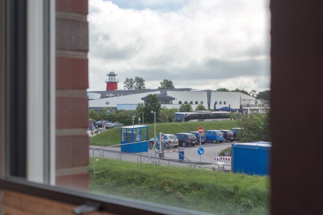 Aus dem Fenster ist ein roter Leuchtturm und ein Parkplatz mit Autos sichtbar.