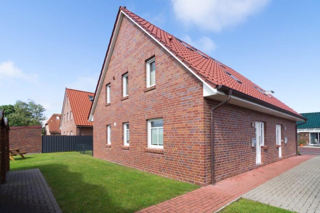 Rotes Ziegelhaus mit Garten und Terrasse unter blauem Himmel.