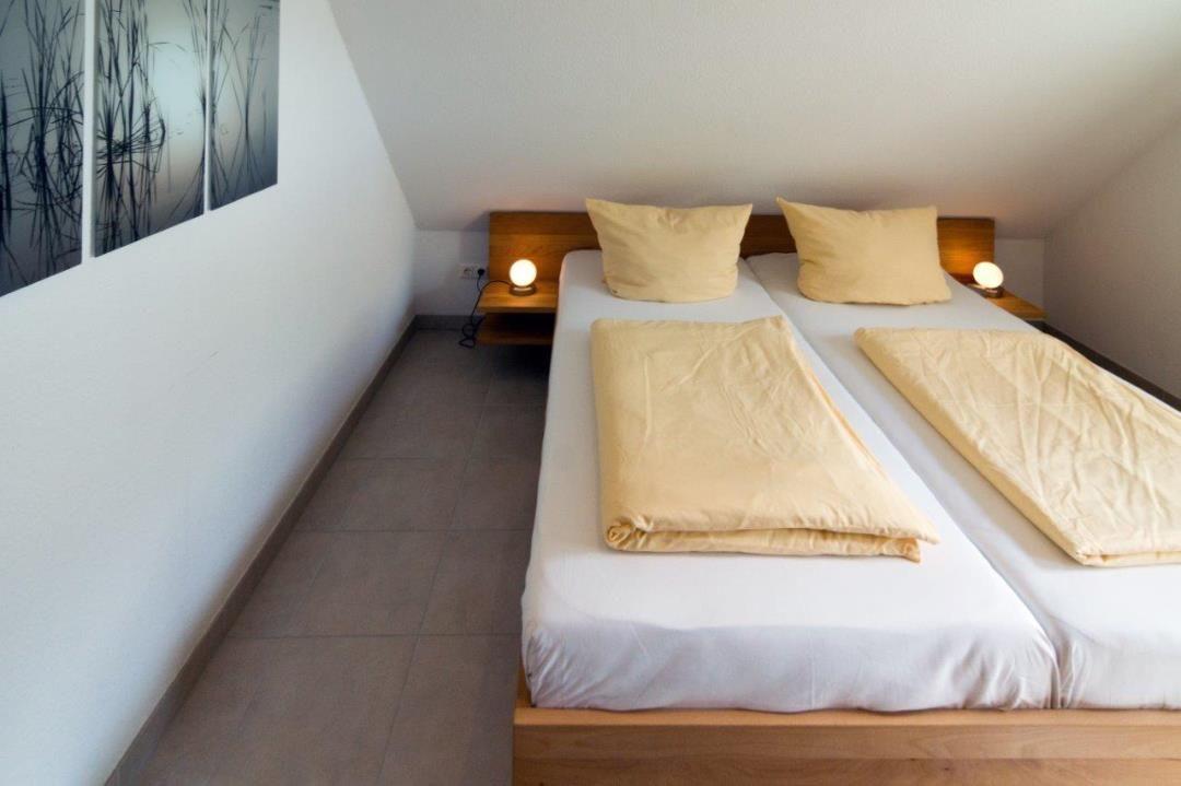 Zimmer mit Doppelbett, Holzgestell und zwei Nachttischen mit Lampen.