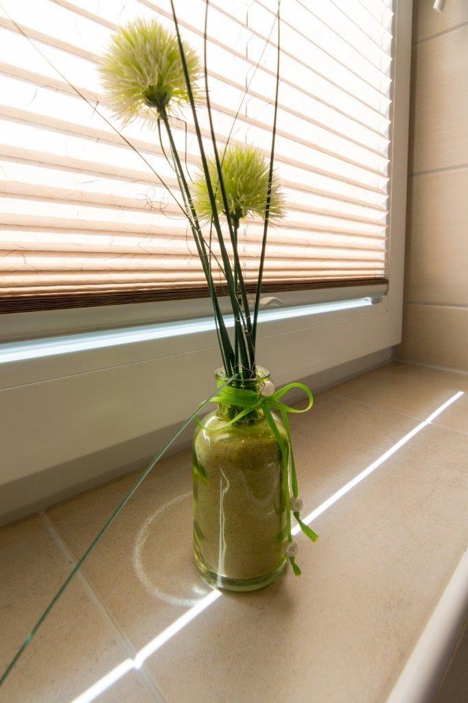 Glasvase mit grünen Blumen auf Fensterbank