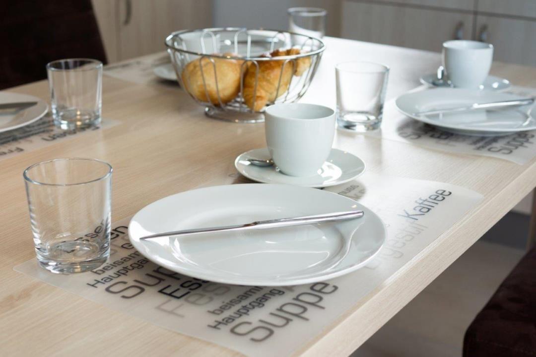 Tisch mit Tassen, Tellern und Brötchen auf Untertellern mit Text.