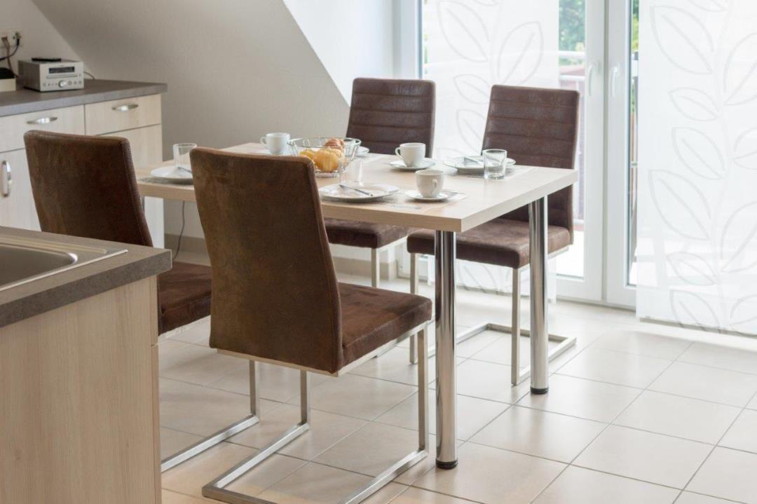 Essbereich mit Tisch und vier Stühlen, Küchenzeile und Glasfront.