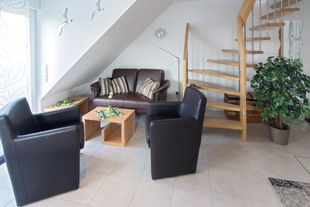 Wohnzimmer mit Sofa, zwei Sesseln, Tisch und Holztreppe