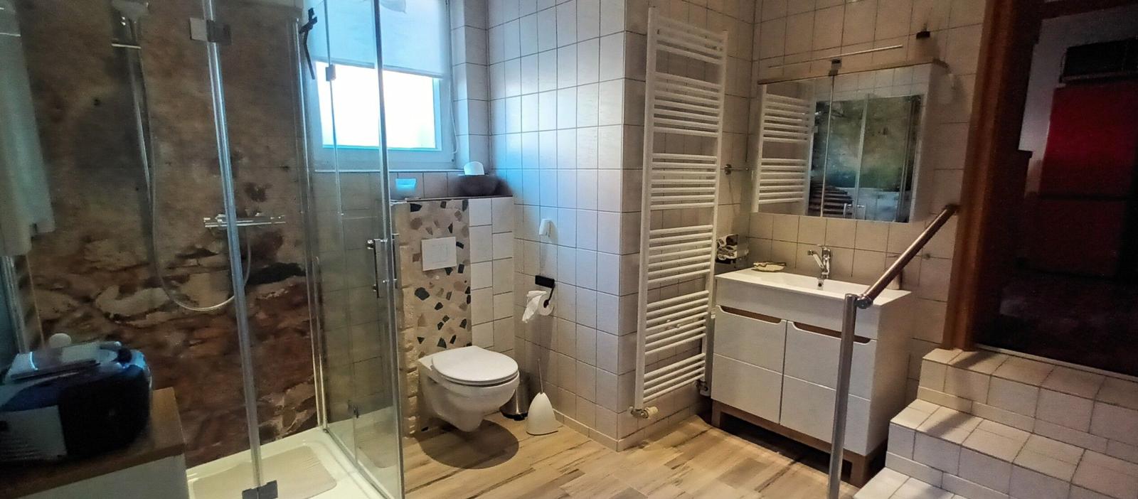 Badezimmer mit Wandheizkörper und Waschtisch, daneben der Treppenaufgang mit 3 Stufen und Geländer