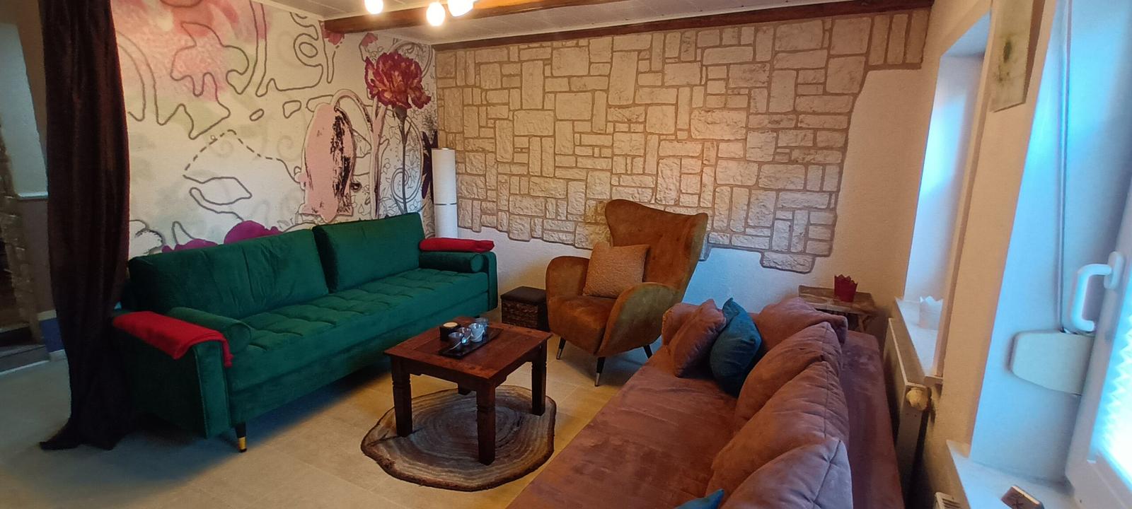 Wohnzimmer mit grünem Sofa, braunem Sessel und Steinwand.
