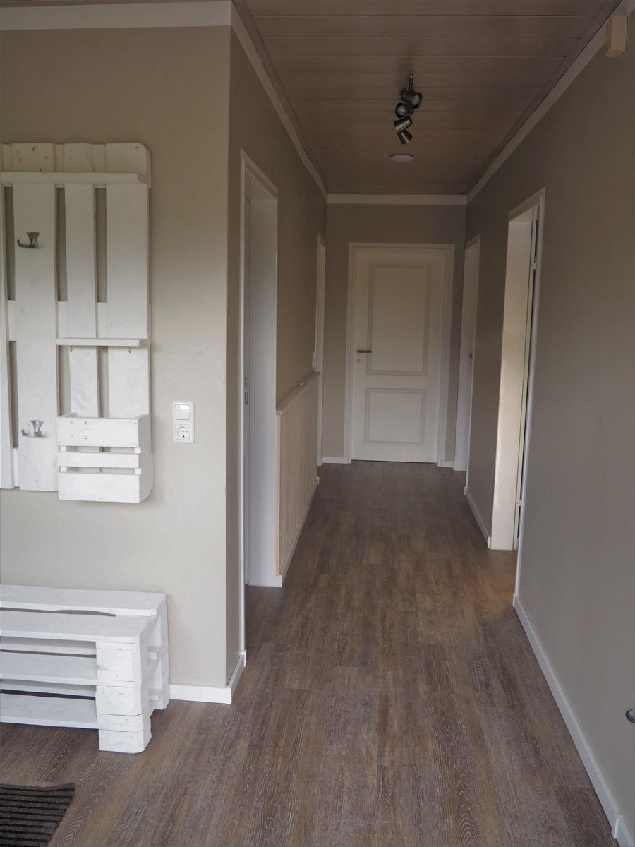 Flur mit Holzboden, weißen Türen und Wandregal aus Holzpaletten.