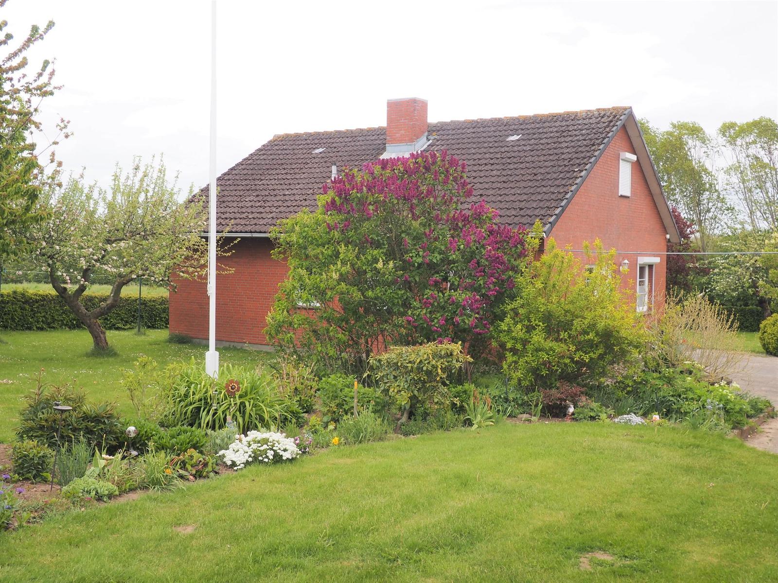 Rotes Backsteinhaus mit Gartenterrasse und blühenden Pflanzen.