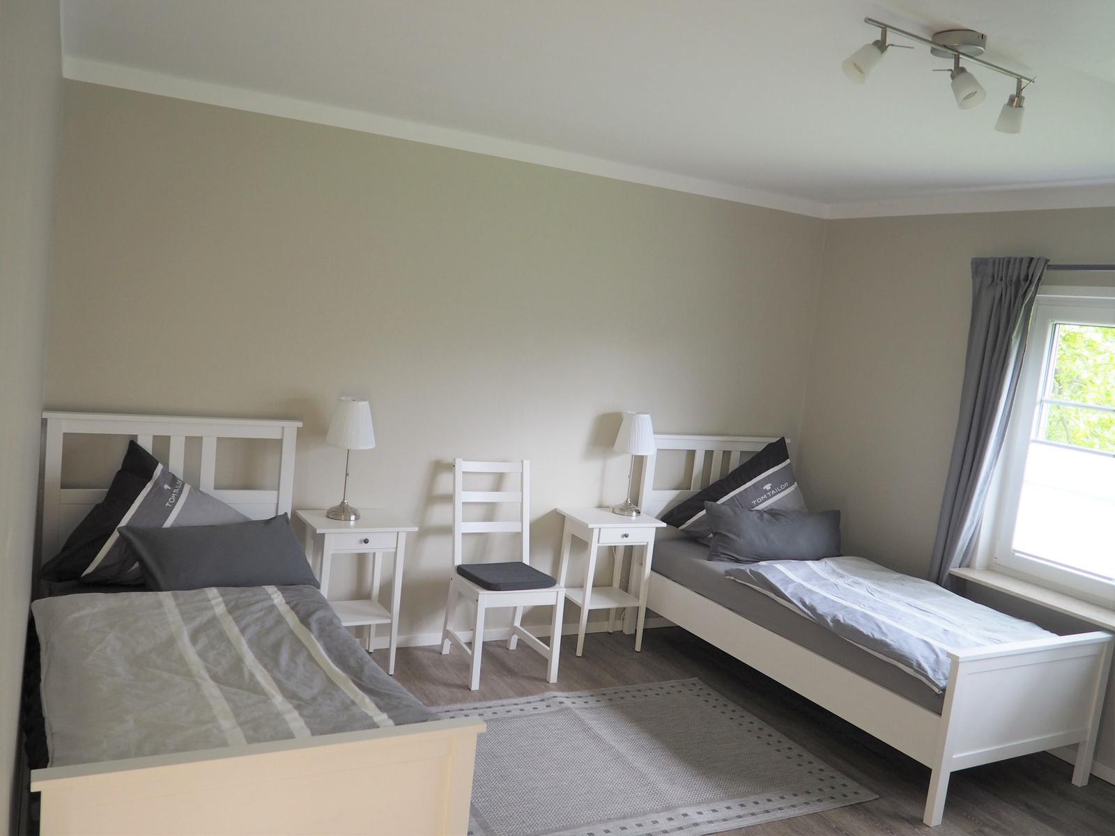 Zwei Einzelbetten, Nachttische, Stuhl und Fenster mit Vorhang.