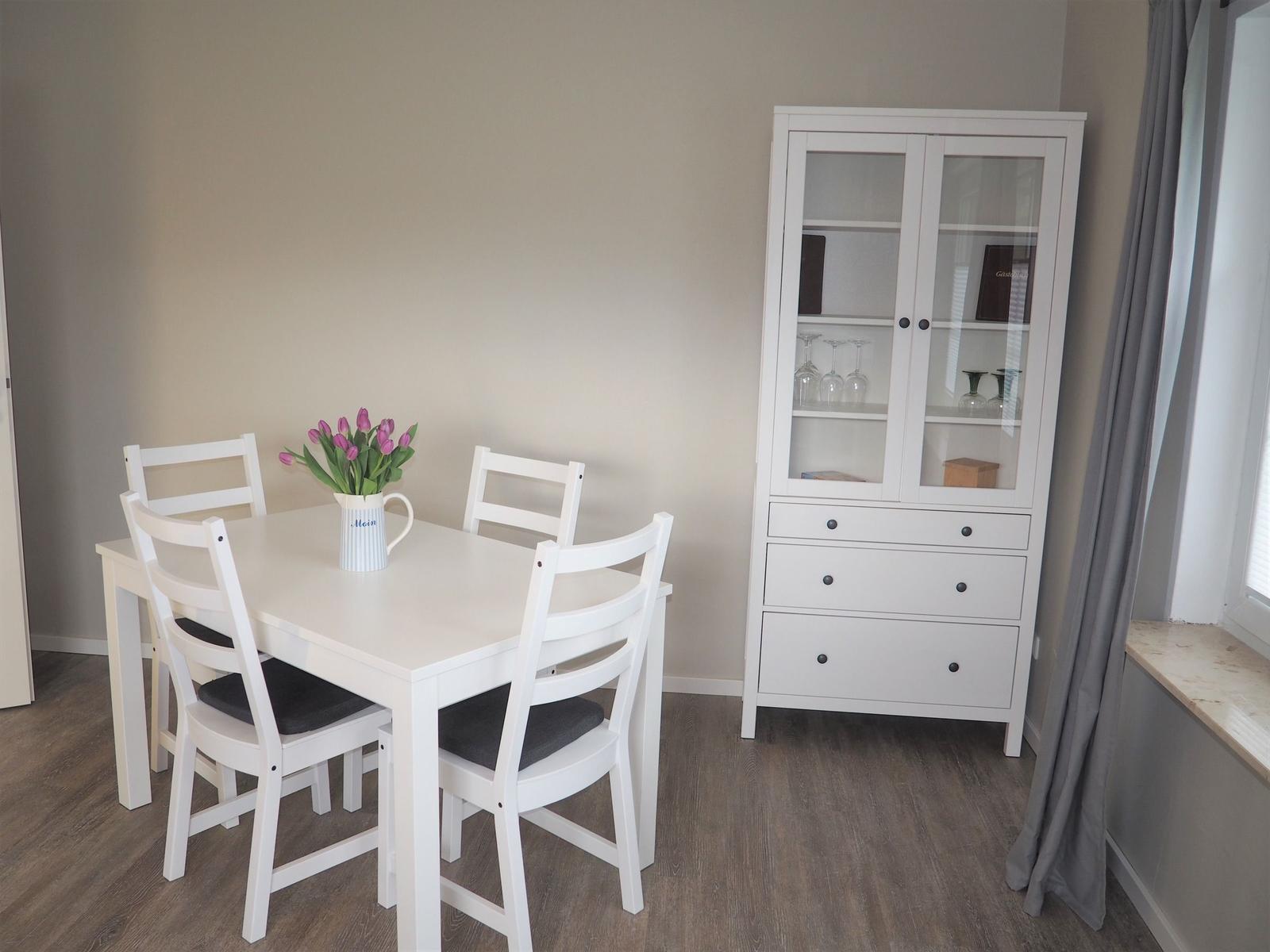 Essbereich mit weißem Tisch, vier Stühlen und Sideboard.