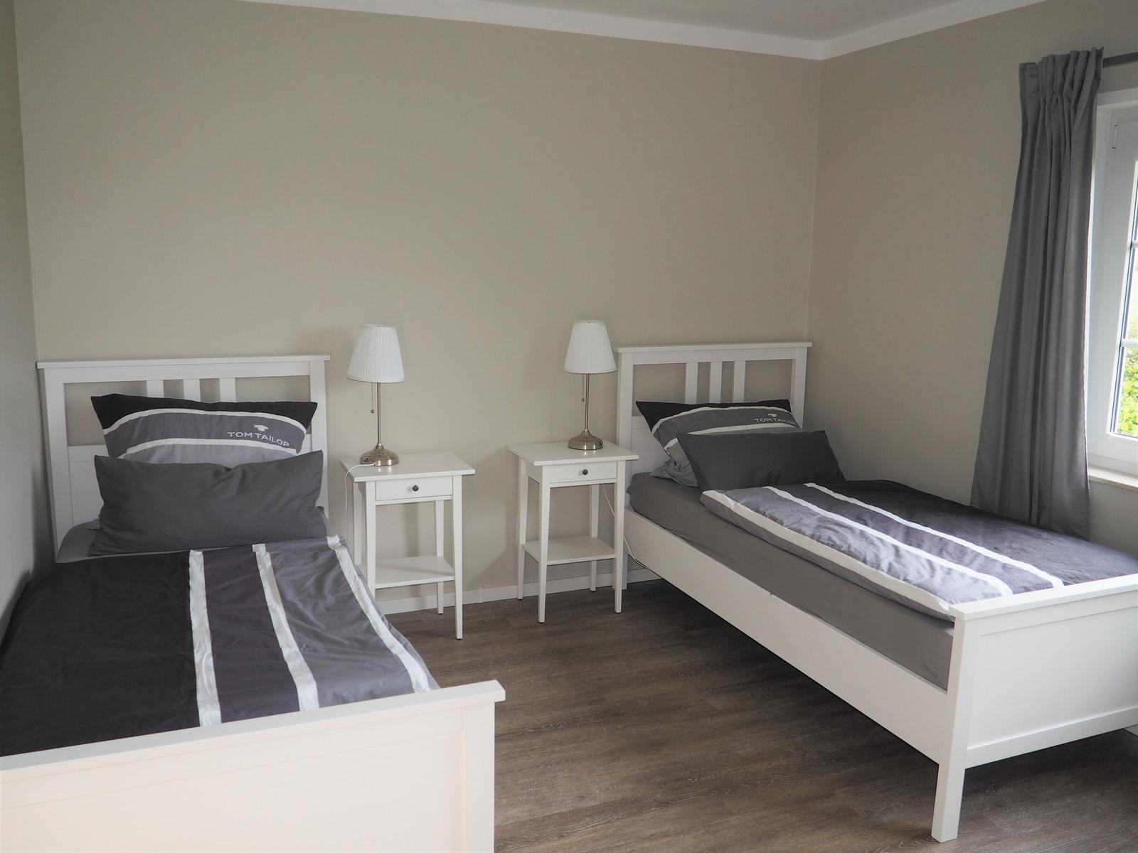 Zwei Einzelbetten mit Nachttischen und Lampen. Fenster mit Vorhang.