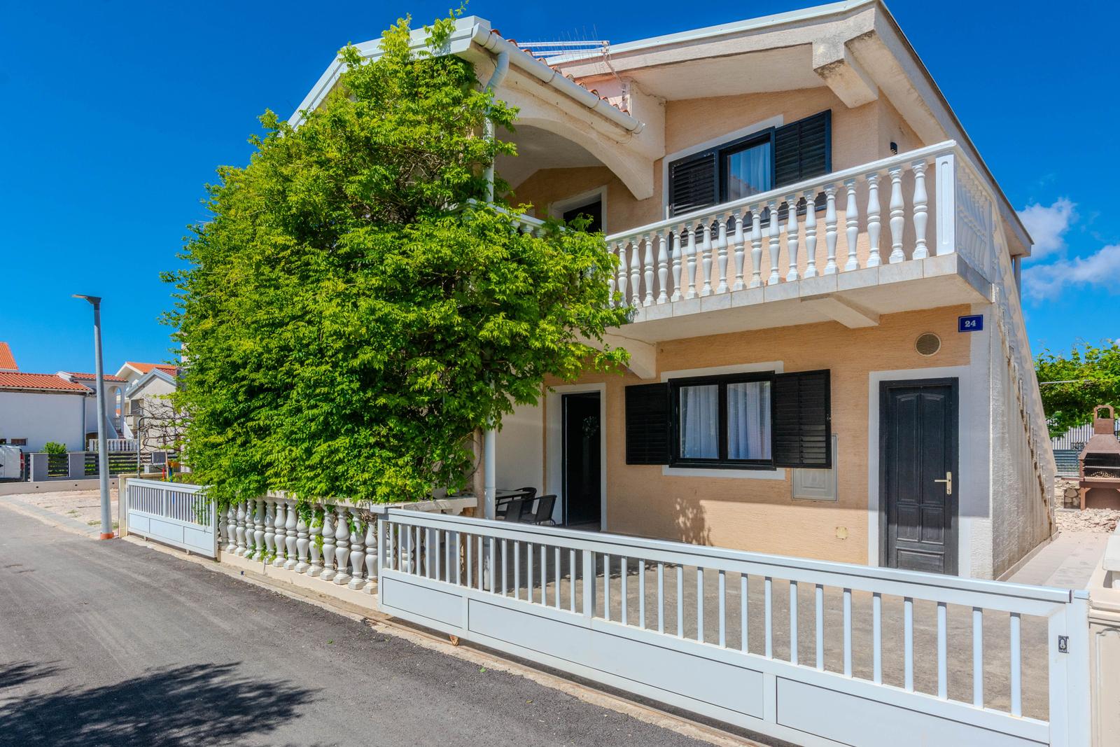 Two-story house with balcony, white railing, and large windows with black shutters.