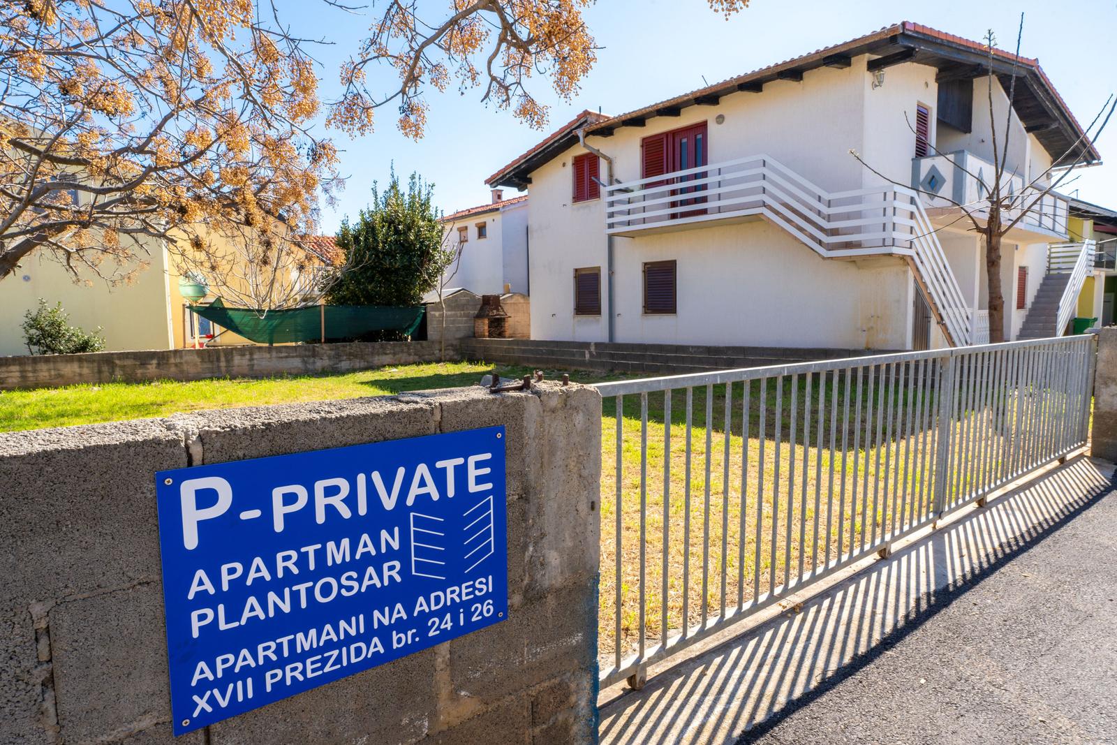 Private apartment building with balcony and garden area. Sign shows address.