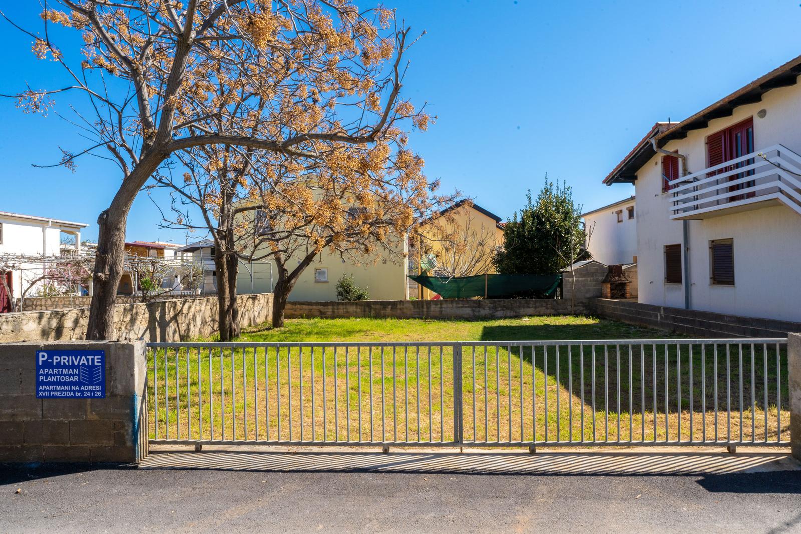Backyard with garden, fence, and tree. House with balcony and windows.