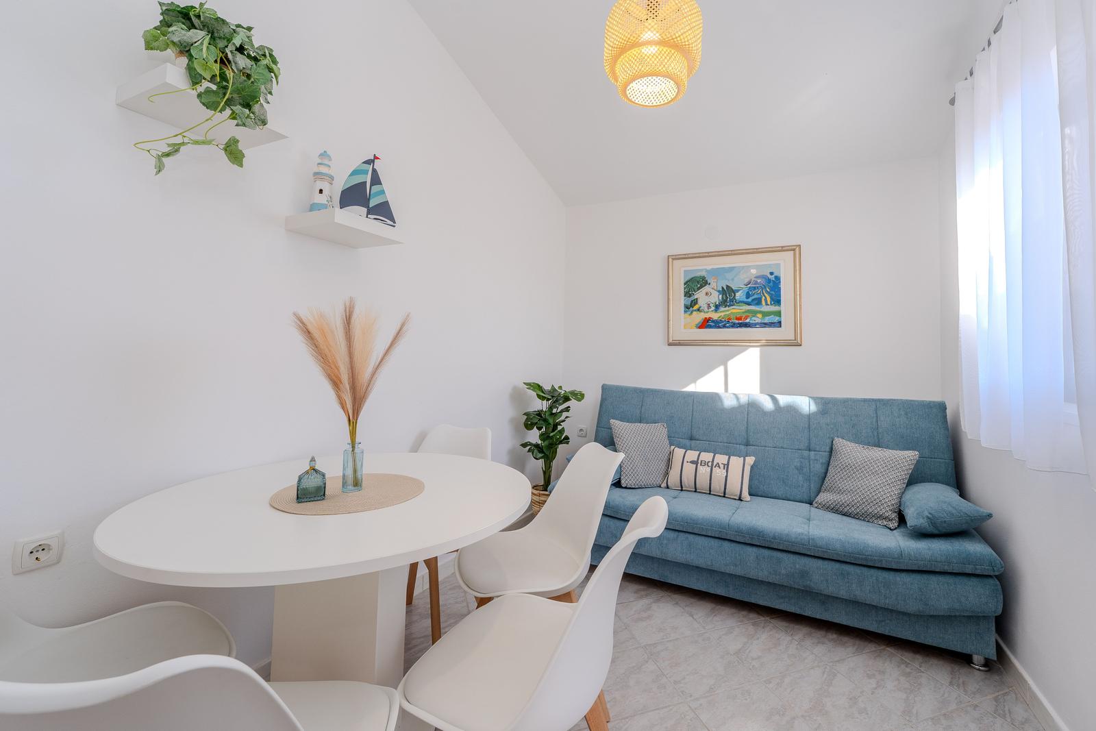 Living and dining area with blue sofa, white table and chairs, and wall shelves.