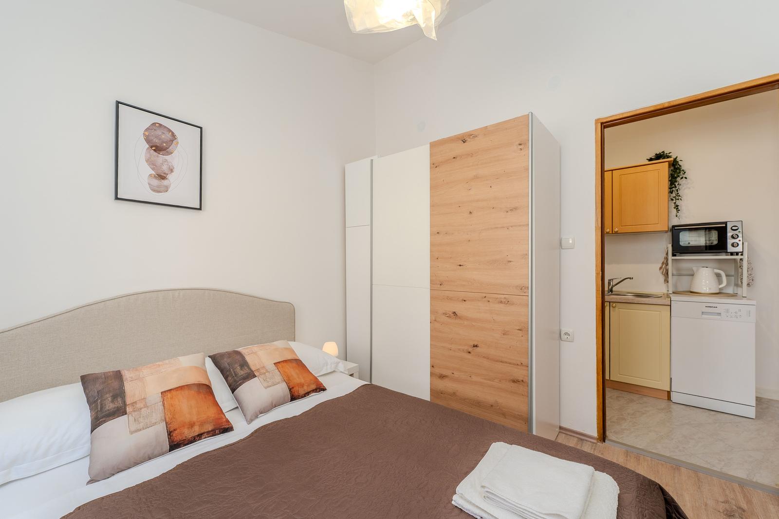 Bedroom with bed, wardrobe, and view into the kitchen.