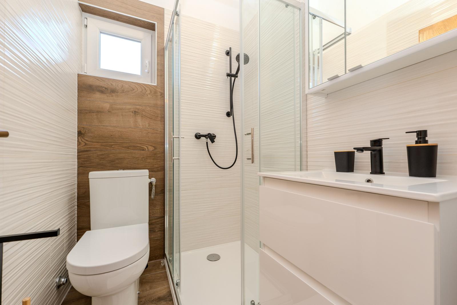 Bathroom with shower, sink and toilet. Wood wall and window.