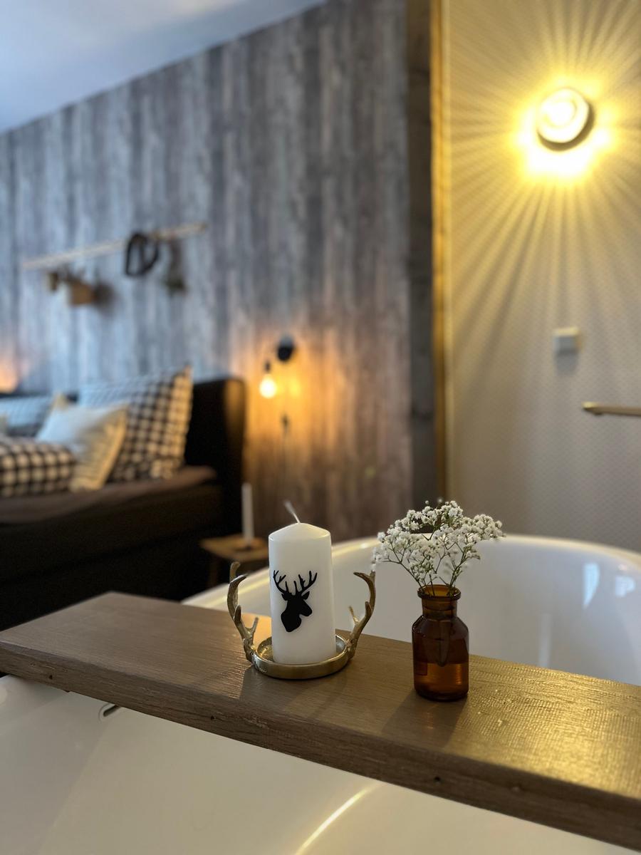 Badewanne mit Kerze und Blumen auf Holzbank