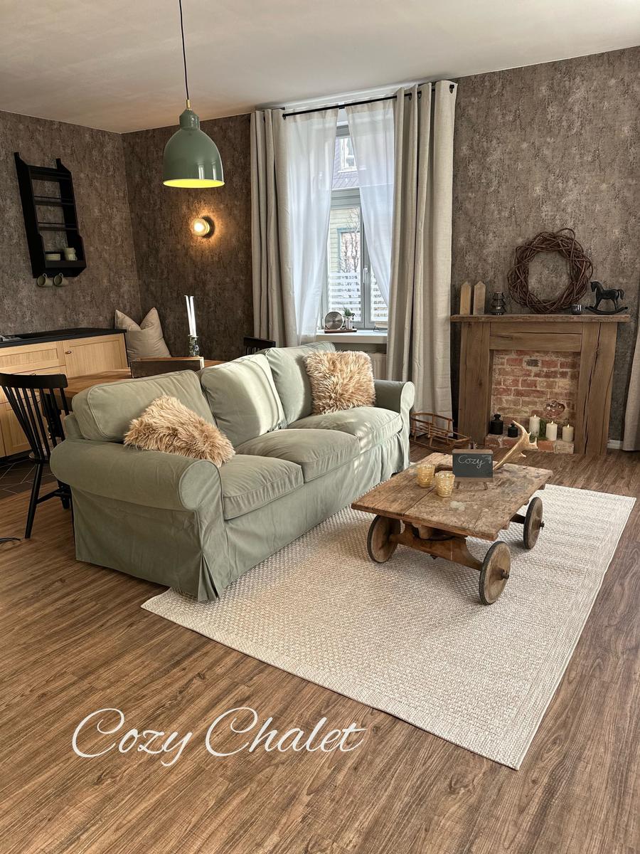 Ein Wohnzimmer mit Sofa, Kamin und Holzboden. An der Wand hängt eine Lampe.