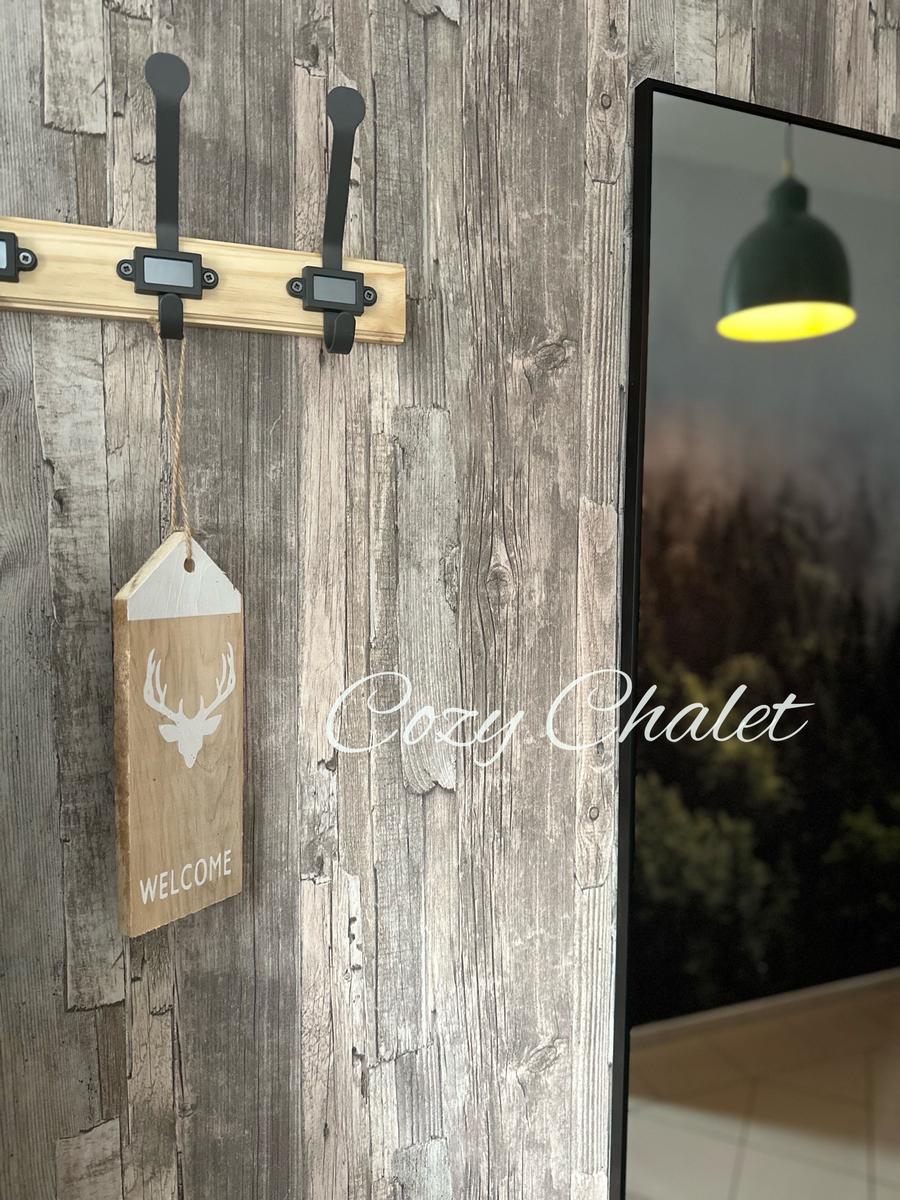 Holzpaneelwand mit Haken und Willkommensschild. Spiegel reflektiert Lampe.