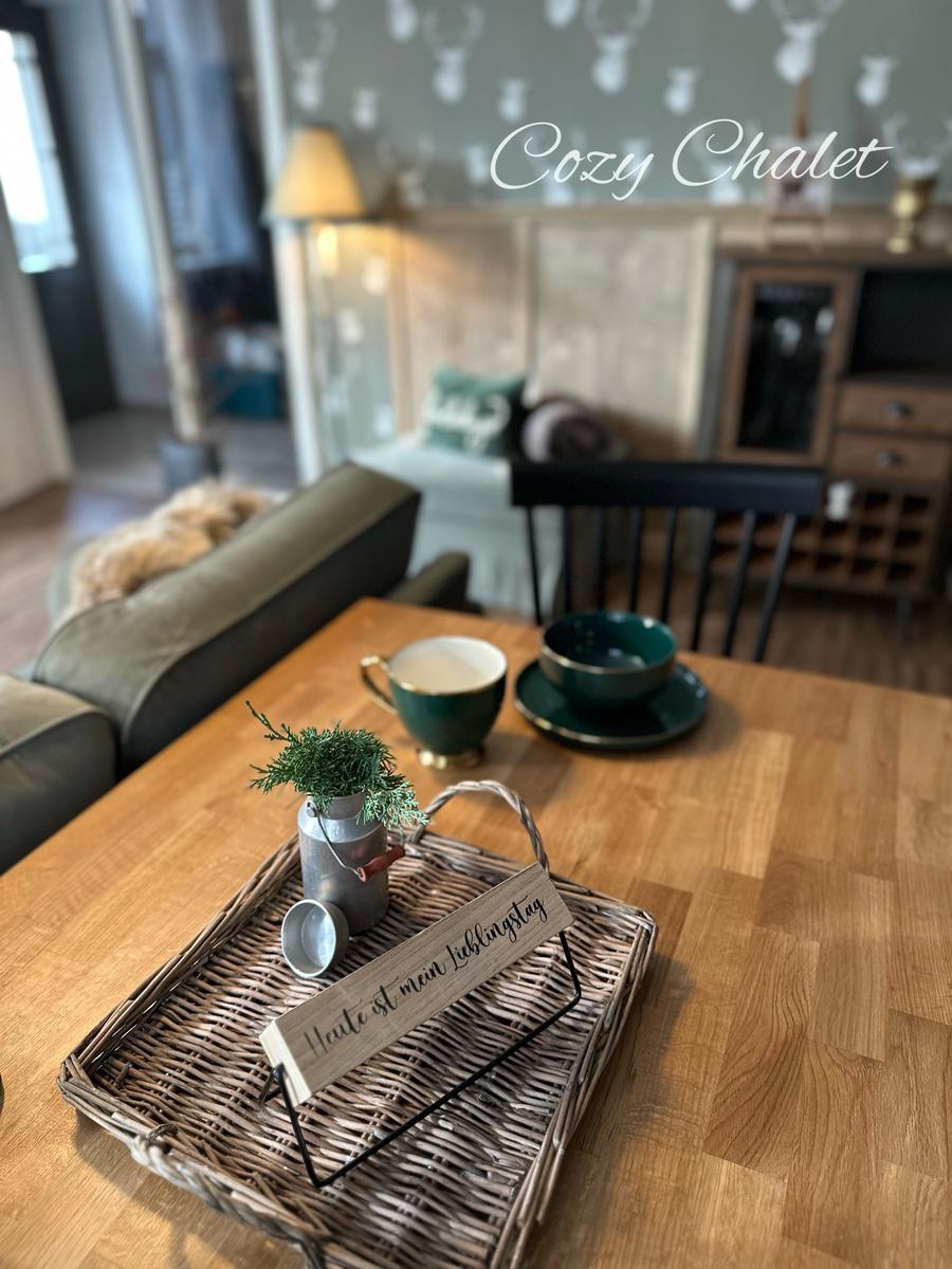 Holztisch mit Korb, Tasse und Schale. Im Hintergrund Sofa und Kamin.