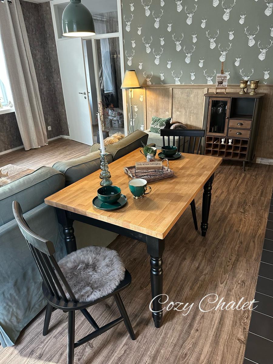 Essbereich mit Holztisch, Stühlen und dekorativer Wandtapete mit Hirschmotiven.