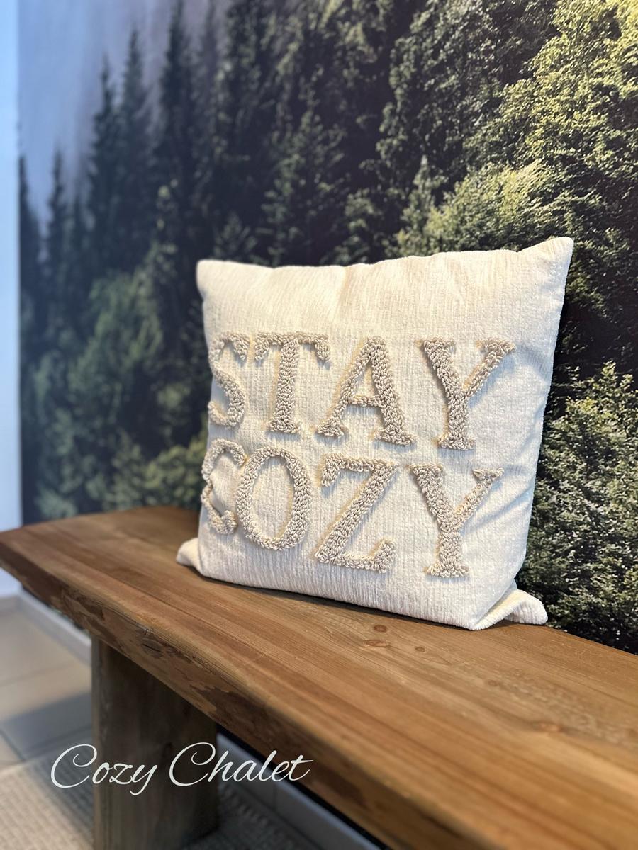 Kissen mit Aufschrift STAY COZY auf Holzbank vor Waldtapete