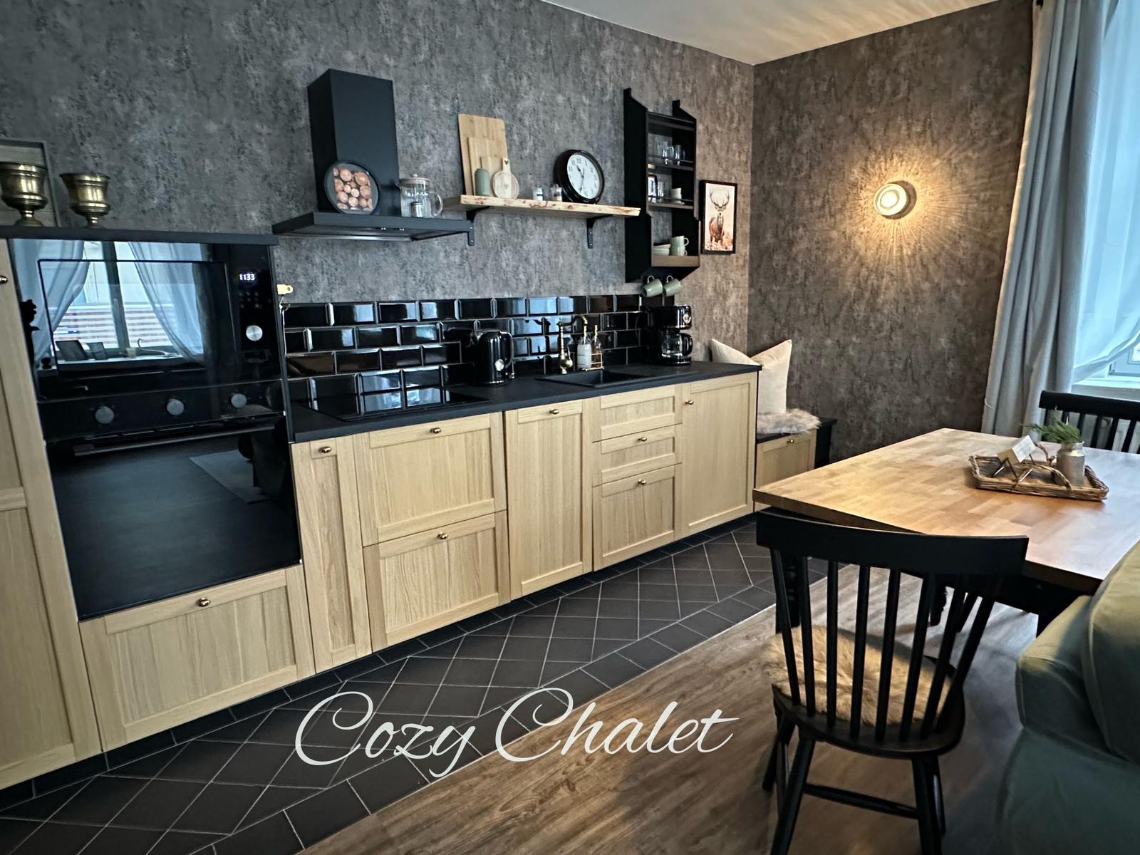 Küche mit Holzschränken, schwarzer Arbeitsplatte und Essbereich mit Holztisch.