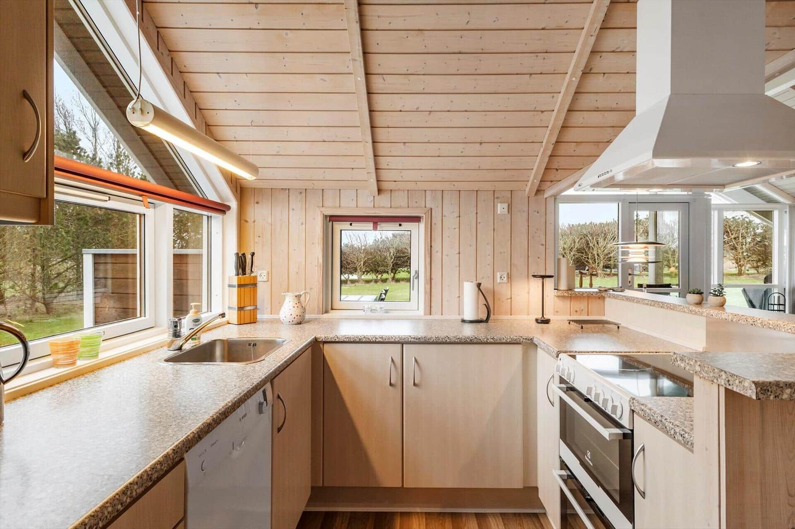 Küche mit Holzwand und -decke, Fenster, Arbeitsplatten und Geräten.