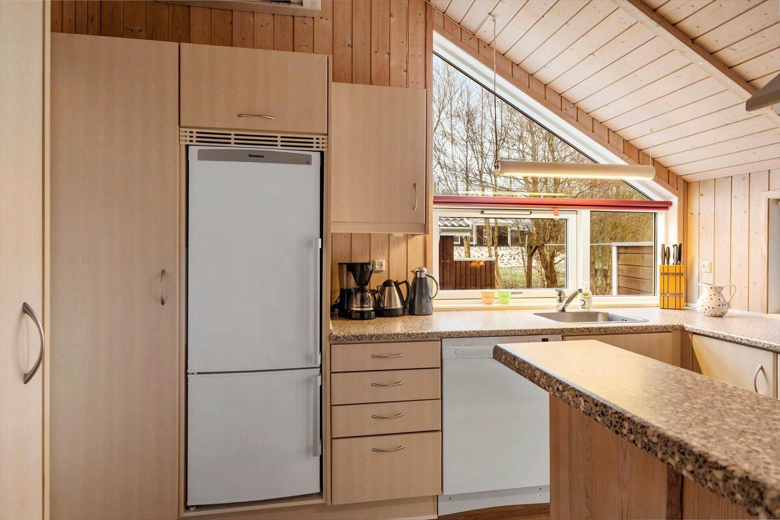 Küche mit Kühlschrank, Spüle und Fenster. Holzwände und Arbeitsplatte.