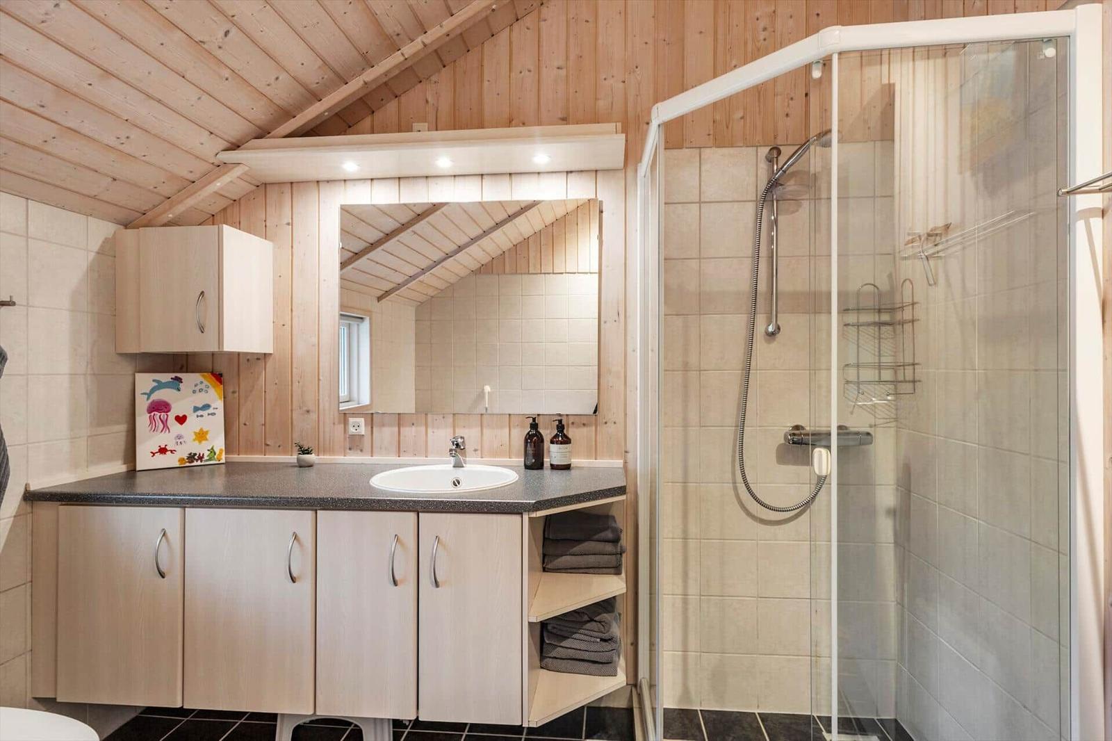 Badezimmer mit Dusche, Waschbecken und Spiegel unter Holzdecke.