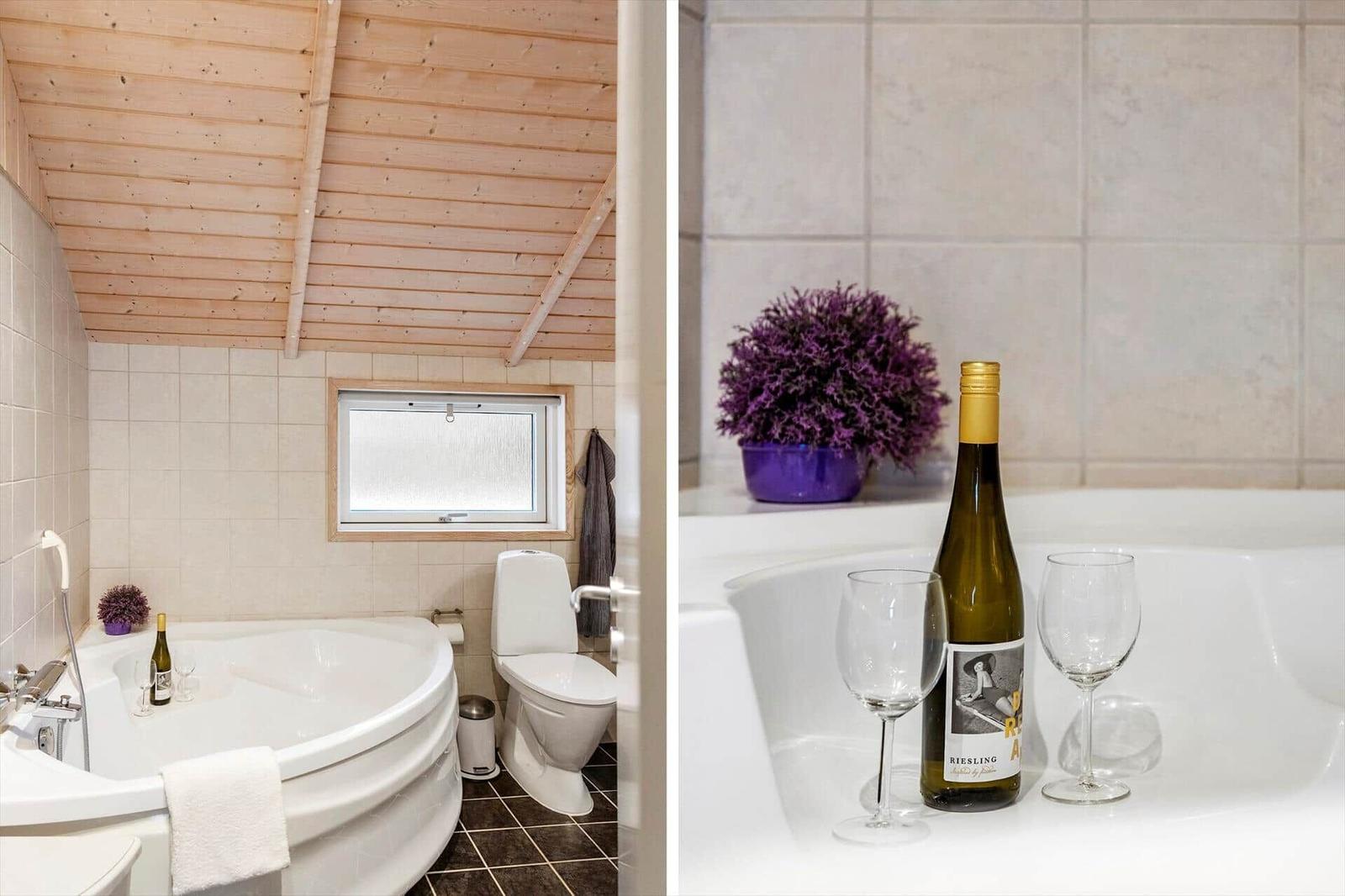 Bad mit Whirlpool, Toilette und Holzdecke. Weißer Whirlpool mit Wein und Pflanze.