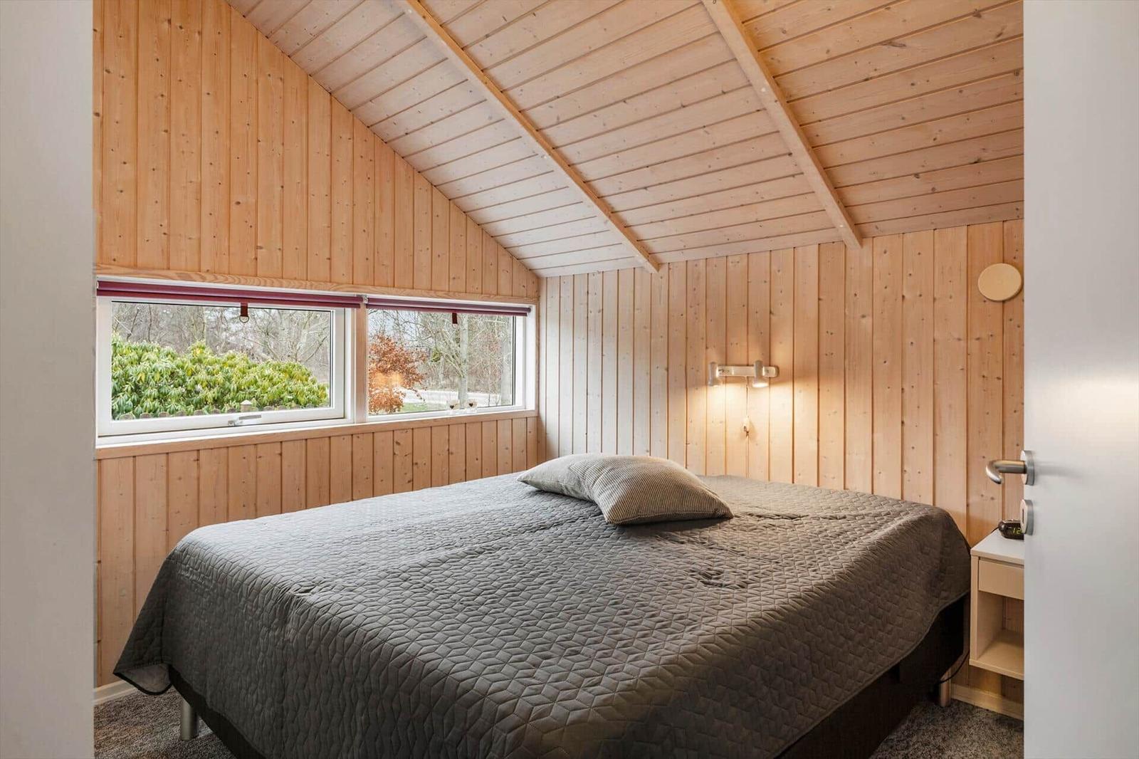 Schlafzimmer mit Holzwand und Dachfenster. Bett mit grauer Bettdecke.