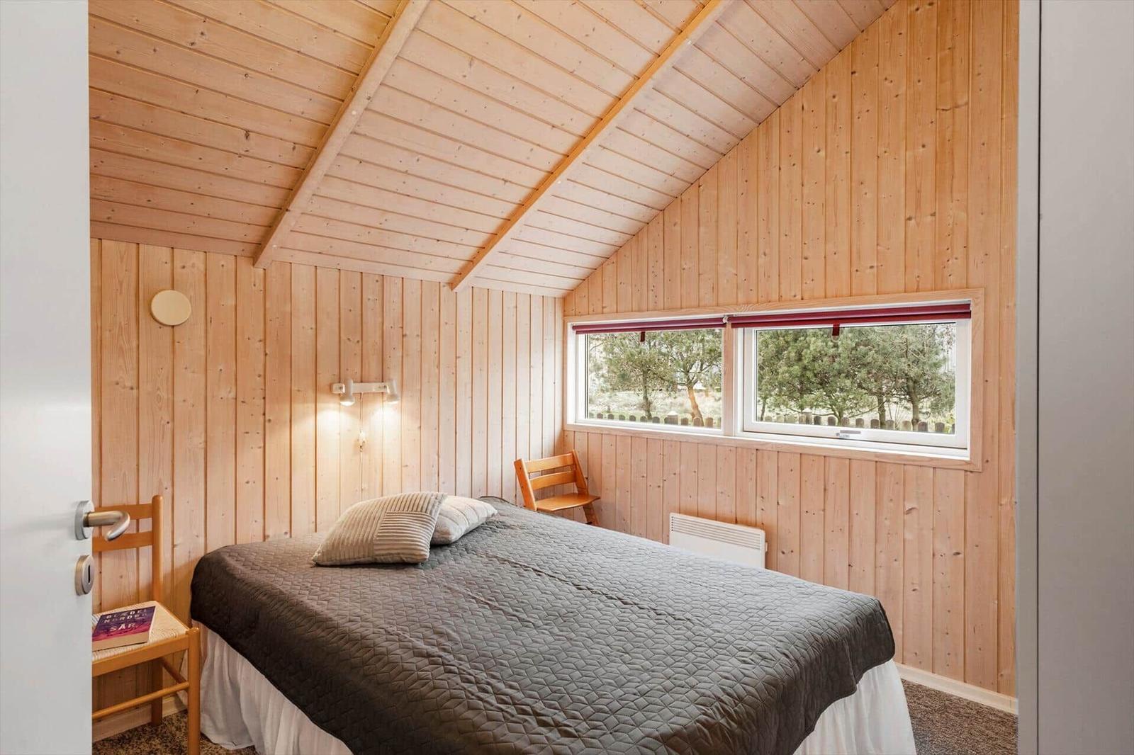 Schlafzimmer mit Holzwand, Bett, Stuhl und Fenster zum Garten.