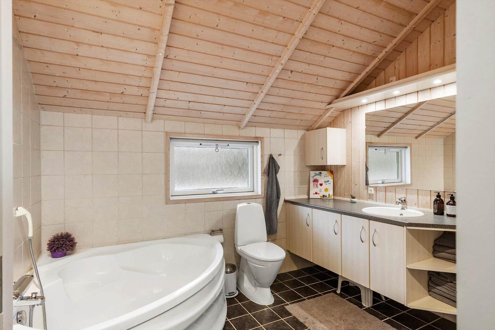 Badezimmer mit Badewanne, Toilette und Waschbecken unter Holzdecke.